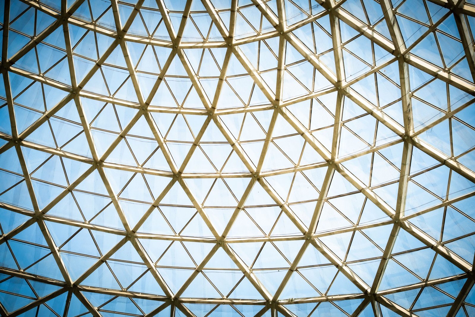 Abstract view of a geometric glass dome with clear blue sky showing modern architectural design.